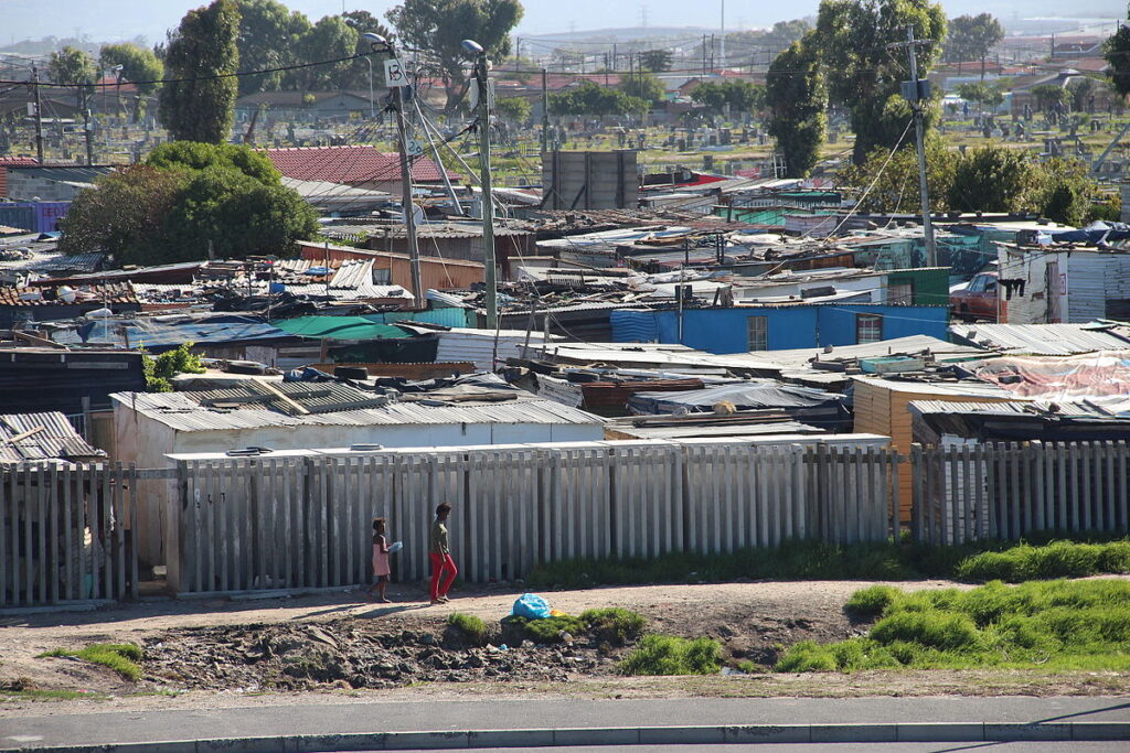 Two children walking with shacks in the back ground.